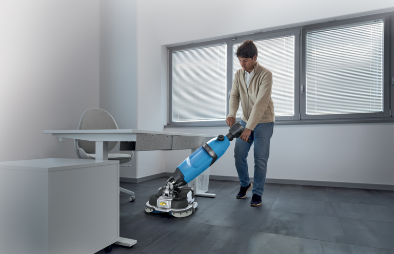 CONQUEST_HDS45 UPRIGHT FLOOR SCRUBBER_UNDER TABLE CLEANING - Conquest - Conquest Man operating a blue floor-polishing machine in an office, standing beside a desk and chair by large windows with blinds.Man operating a blue floor-polishing machine in an office, standing beside a desk and chair by large windows with blinds.Man operating a blue floor-polishing machine in an office, standing beside a desk and chair by large windows with blinds.Man operating a blue floor-polishing machine in an office, standing beside a desk and chair by large windows with blinds.