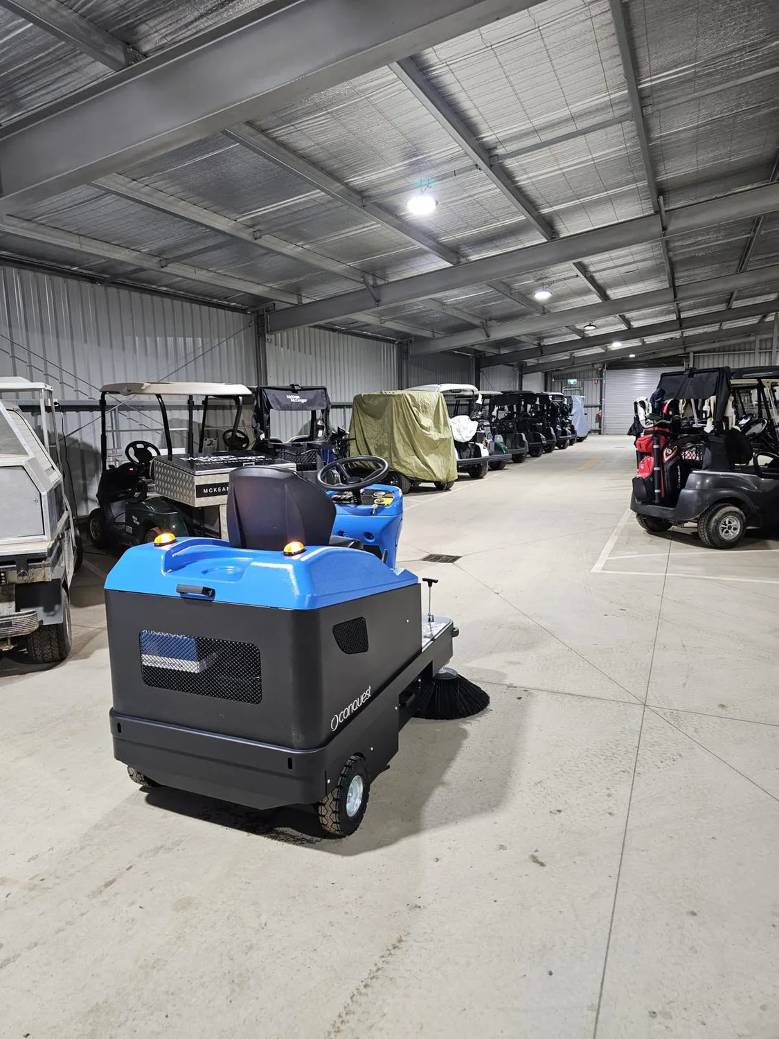 Conquest HD90 ride on sweeper cleaning a golf cart storage shed, providing efficient dust and debris collection on hard floors