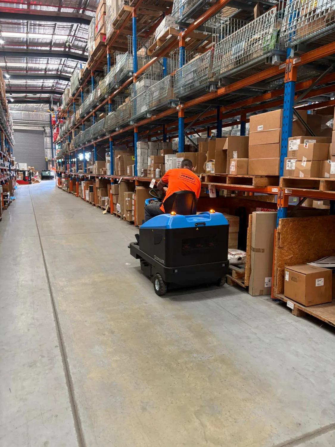 Conquest HD90 ride on sweeper operated in a warehouse aisle, delivering efficient dust control and industrial floor cleaning