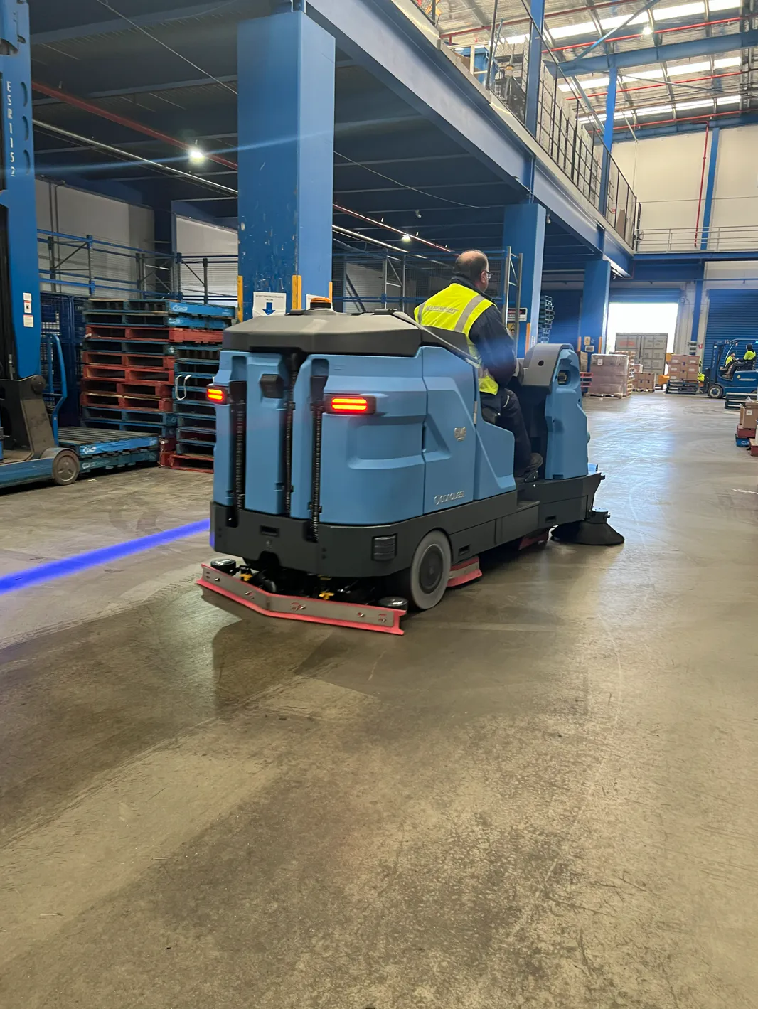 Conquest HDC170 combination sweeper scrubber cleaning warehouse aisles while sweeping and scrubbing floors