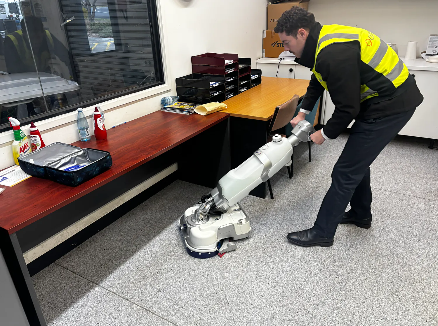 Conquest HDS46 walk-behind floor scrubber cleaning beneath office desks with a compact design for tight spaces