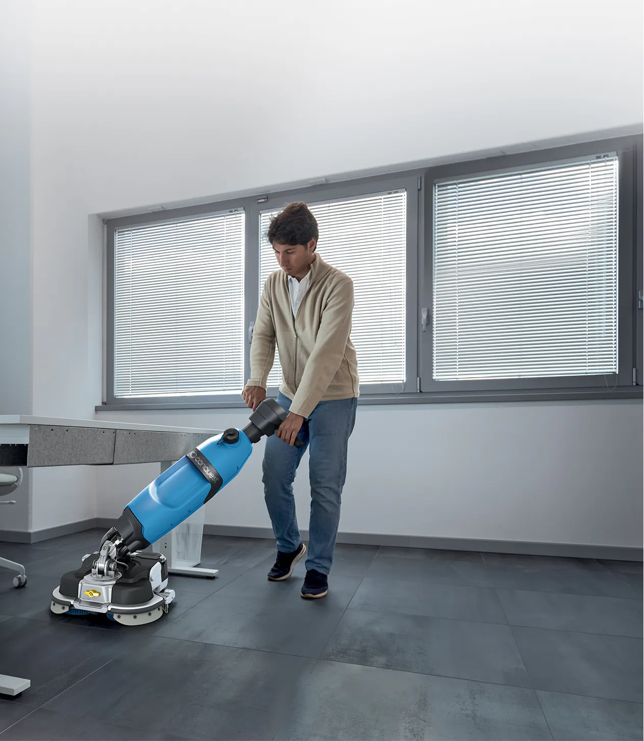 Conquest HDS46 walk-behind floor scrubber cleaning beneath office furniture with its low-profile cleaning head