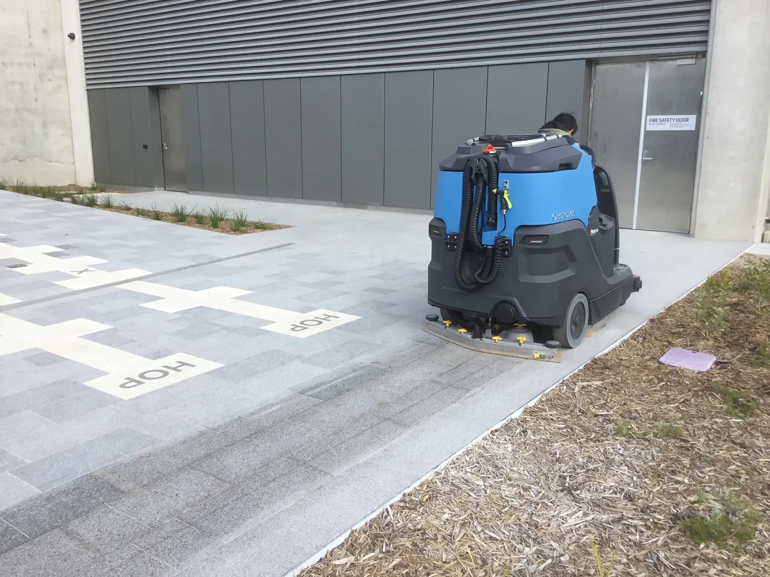 Conquest HDS90 ride-on floor scrubber cleaning outdoor flooring at a metro train station entrance