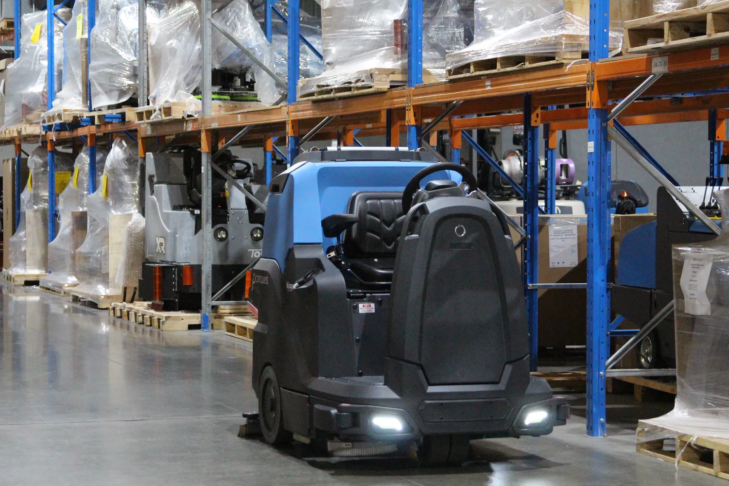Conquest HDS90 ride-on floor scrubber cleaning warehouse aisles for efficient industrial floor maintenance