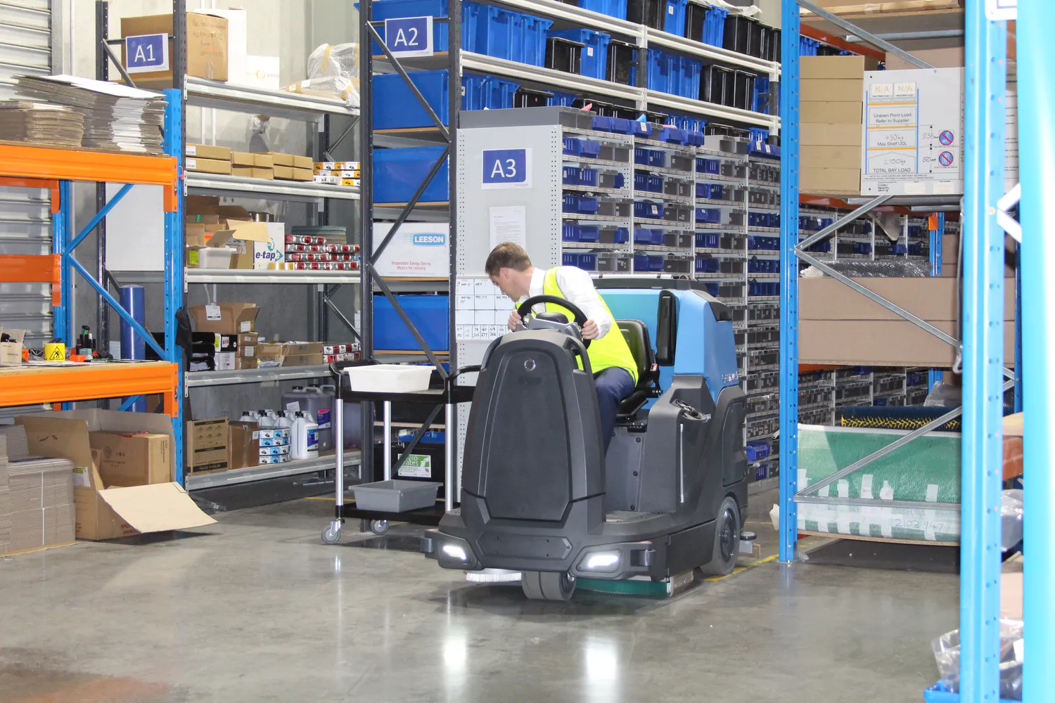 Operator using the Conquest HDS90 ride-on floor scrubber to clean warehouse floors in an industrial facility