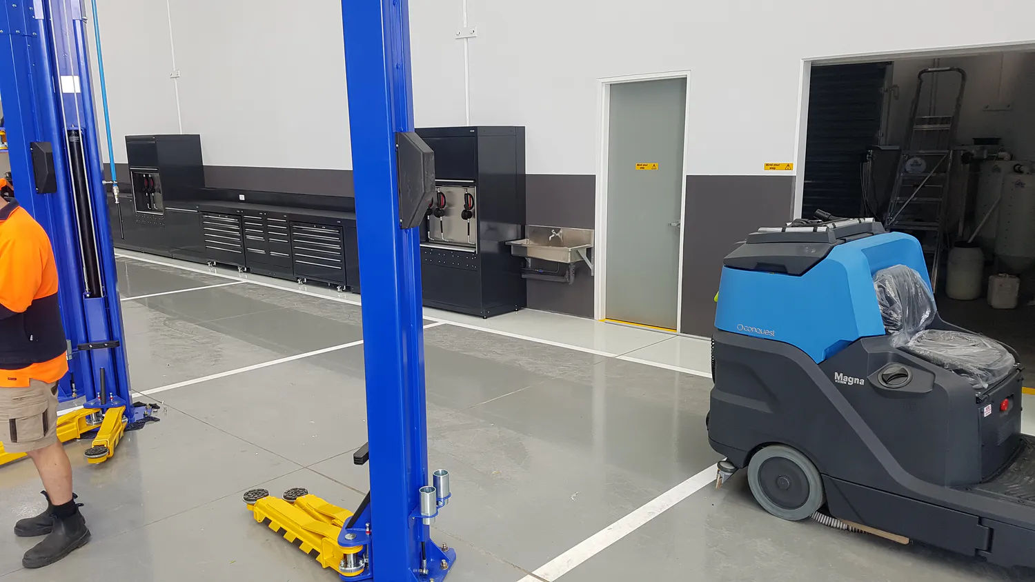 Conquest HDS90 Ride-On Industrial Scrubber cleaning concrete floors in an automotive workshop