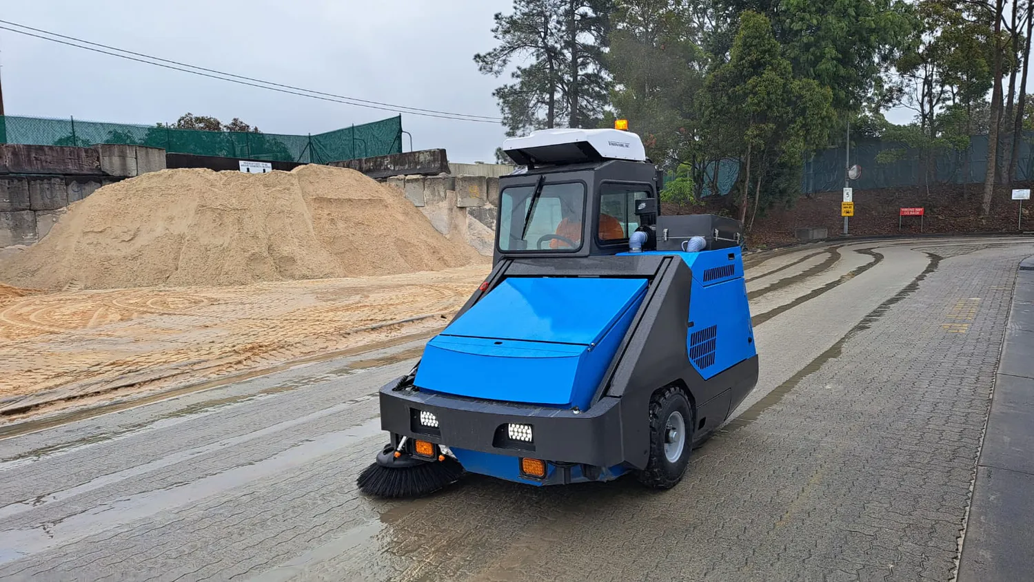 Conquest SD180-HEPA ride-on sweeper cleaning a concrete manufacturing site with enclosed cab and HEPA filtration