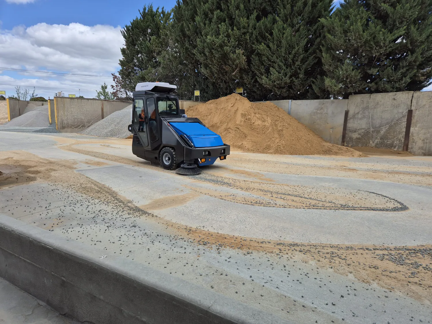 Conquest SD180-HEPA ride-on sweeper removing dust and debris at a construction materials yard with HEPA filtration